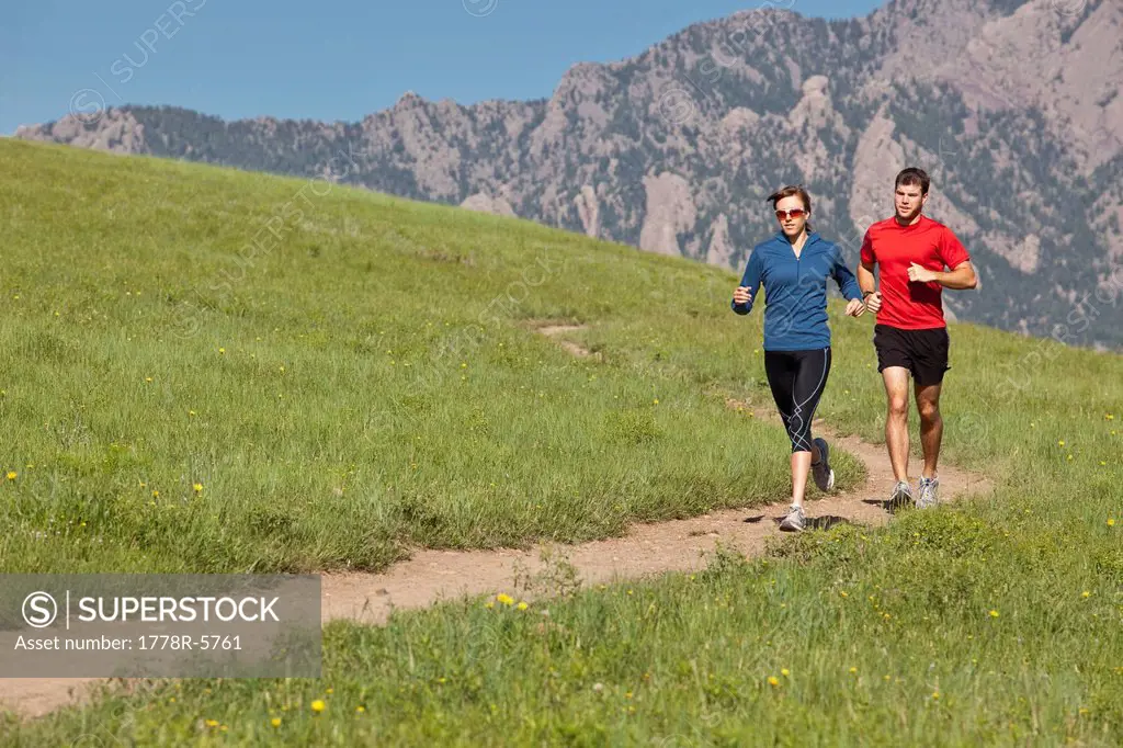 A man and woman run on a grassy trail in the foothills of the Rocky Mountains, Colorado.