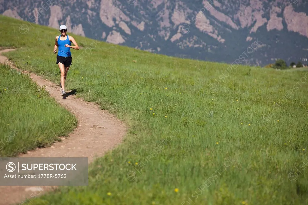 A woman runs on the curving Mesa Trail with the foothills in the background near Boulder, Colorado.