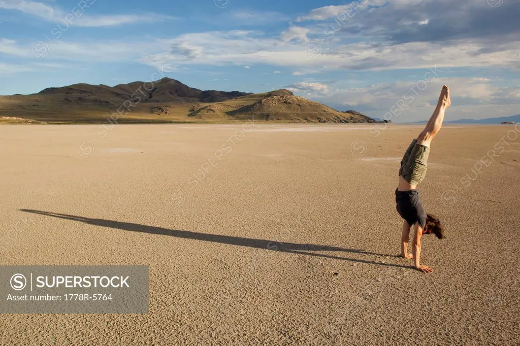 A woman with long shadow practices hand stands on the salt flats of the Great Salt Lake, Utah.