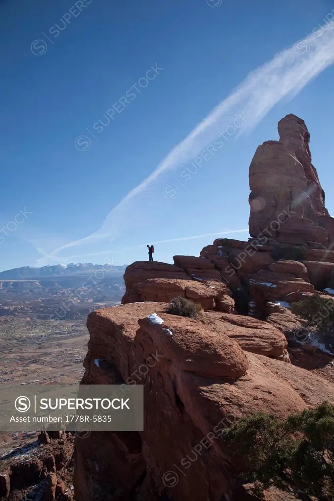 A male hiker standing above a sandstone cliff overlooking Moab, Utah.