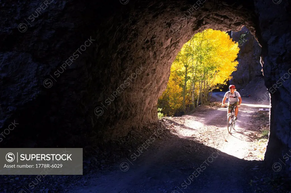 A young man pedals his mountain bike past golden aspen leaves and into a rock tunnel while mountain biking in the San Francisco.