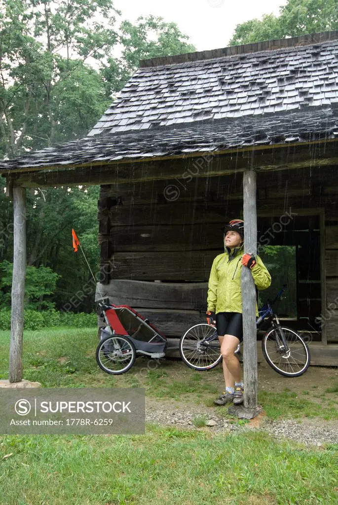 Woman standing under porch roof away from the rain while biking the Blue Ridge parkway, North Carolina.