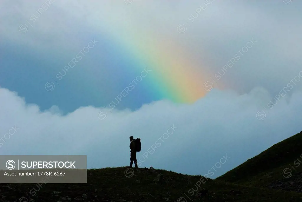 Man standing on ridge in front of rainbow, San Juan National Forest, Colorado silhouette.