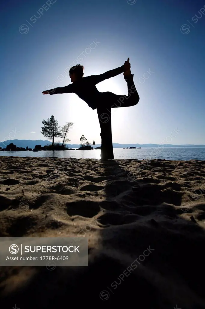 Silhouette of a woman doing yoga on a beach by a lake in the mountains.