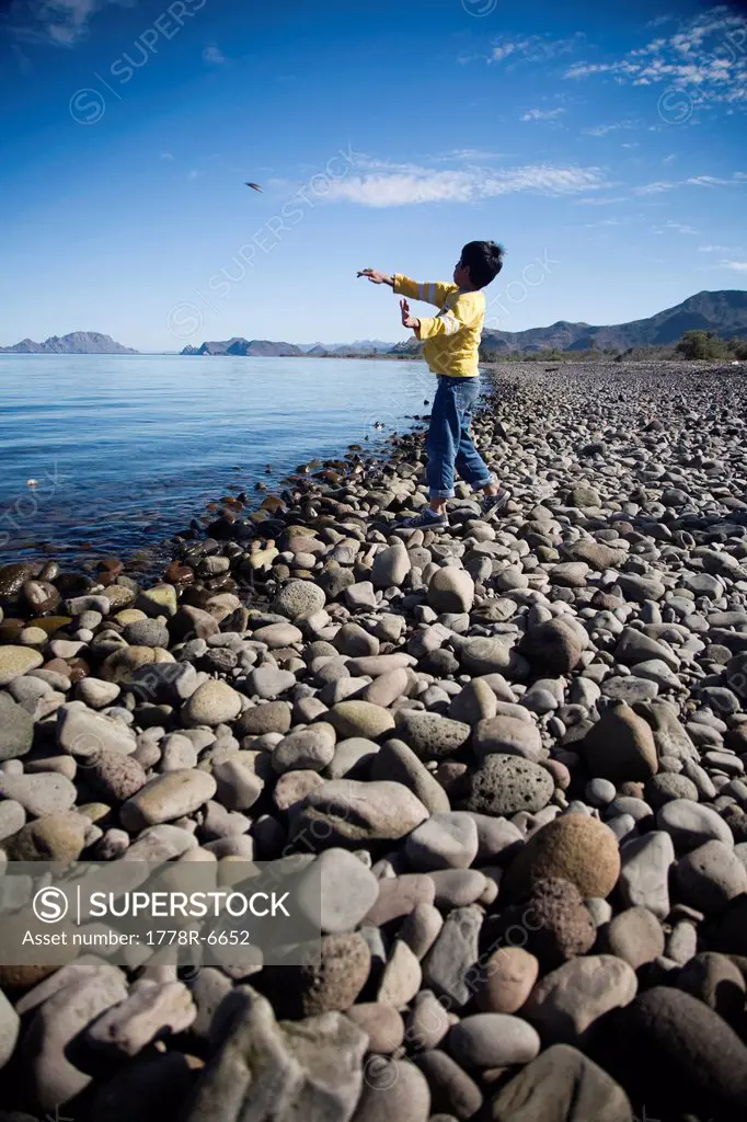 A young boy throws a stone into a large body of water in Loreto, Baja California Sur, Mexico.