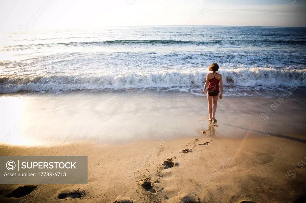A young woman walks away from the camera into the surf on a quiet beach in Sayulita, Mexico.