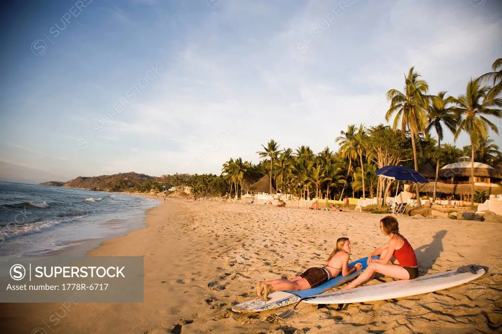 Two young girls sit on their surfboards after surfing near a remote beach in Sayulita, Mexico.