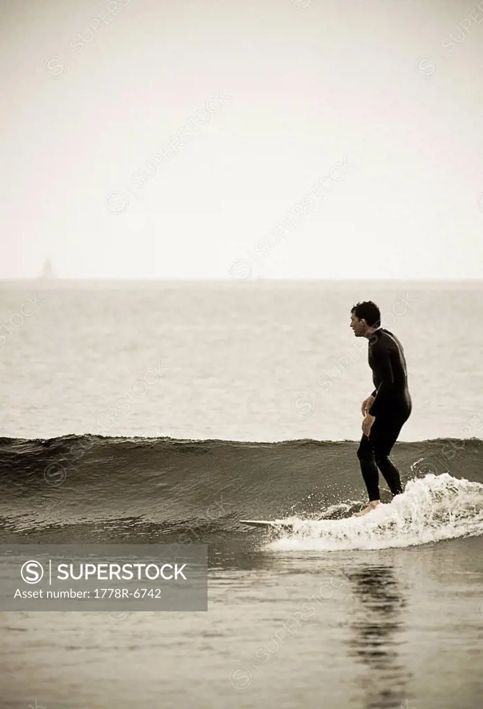 A surfer rides a wave on his longboard desaturated color.