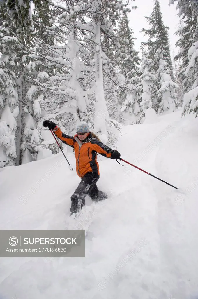 Low angle view of a young woman in snowshoes with ski poles running down a snowshoe trail in deep powder in Bend, Oregon.