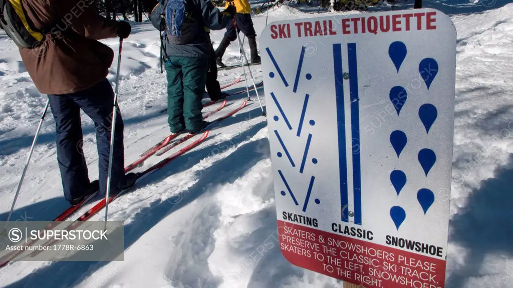Three adults ski past a cross country ski trail etiquette sign in Bend, Oregon.