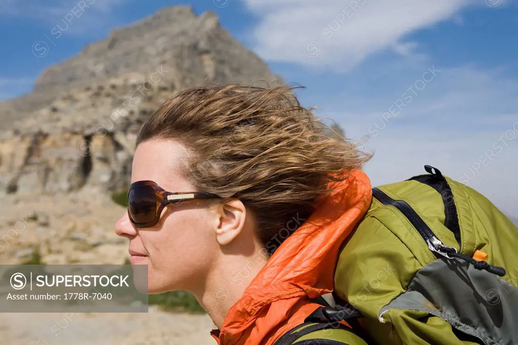 Solo female backpacker enjoying a strong wind blowing through her hair with mountains in background.