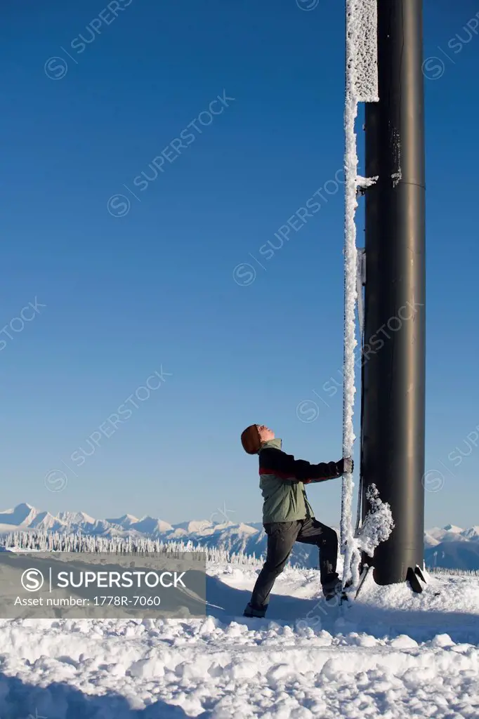 Male teenager climbing a ski lift tower with mountains in background.