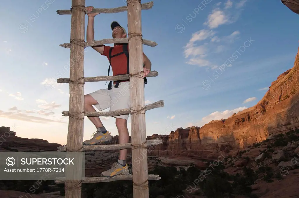 A man climbing a wooden ladder while hiking along a sandstone trail, Canyonlands National Park, Utah.