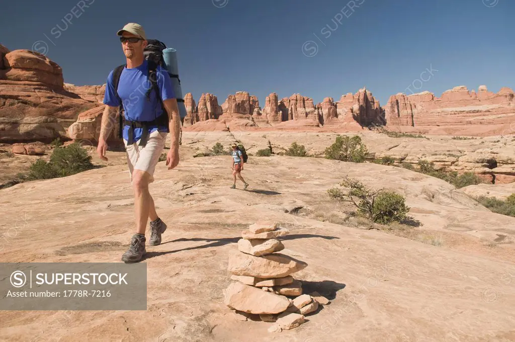 Man and woman hiking along a sandstone trail marked with cairns, Canyonlands National Park, Utah.