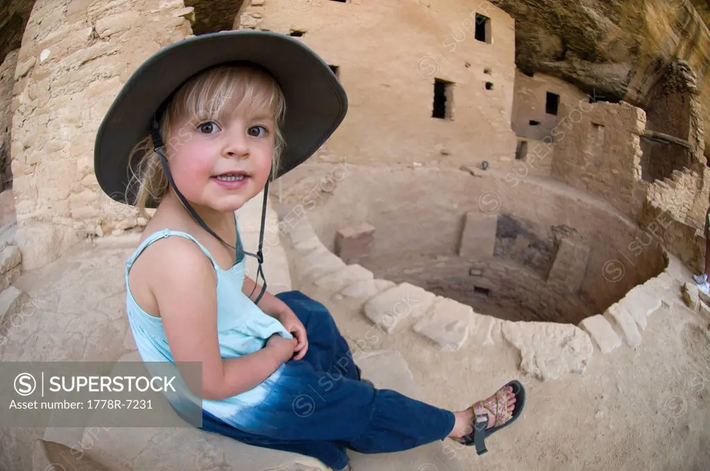 A young girl rests on a stone wall while exploring ruins in Mesa Verde National Park, Cortez, Colorado.