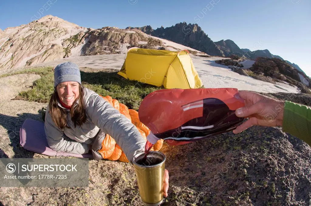 A woman is poured a mug of wine while relaxing at camp, San Juan National Forest, Colorado.