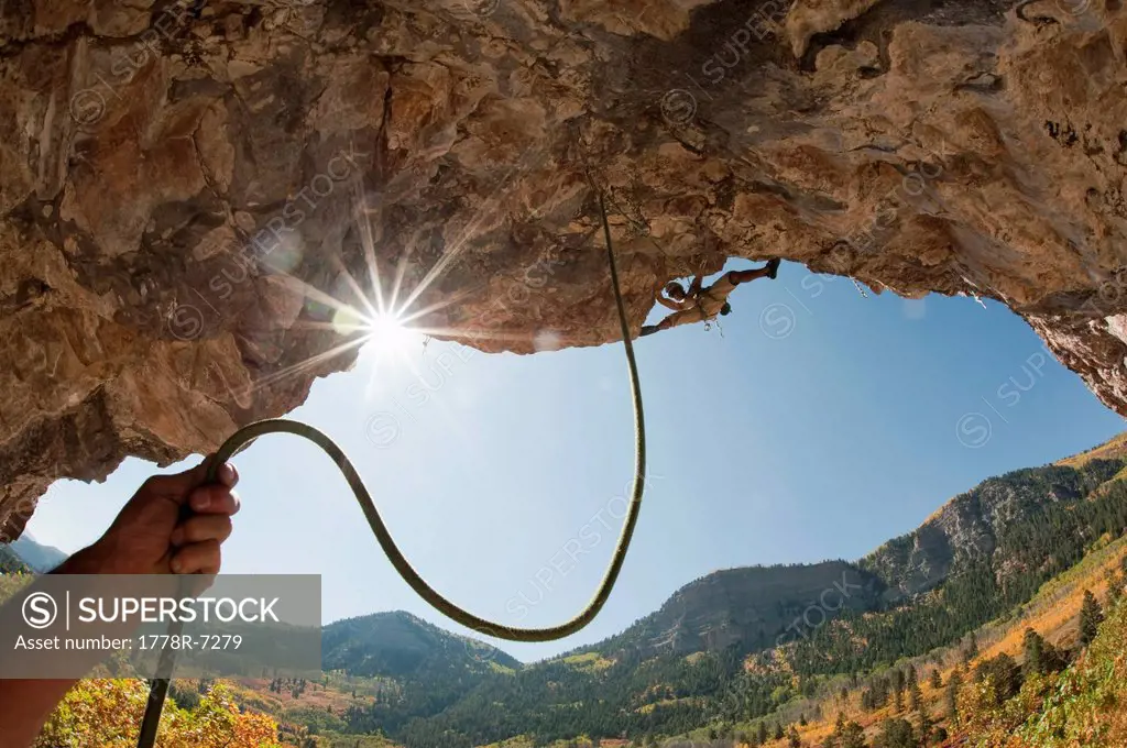 A belayers hand holding rope leading to a man rock climbing at the Golf Wall, San Juan National Forest, Durango, Colorado.