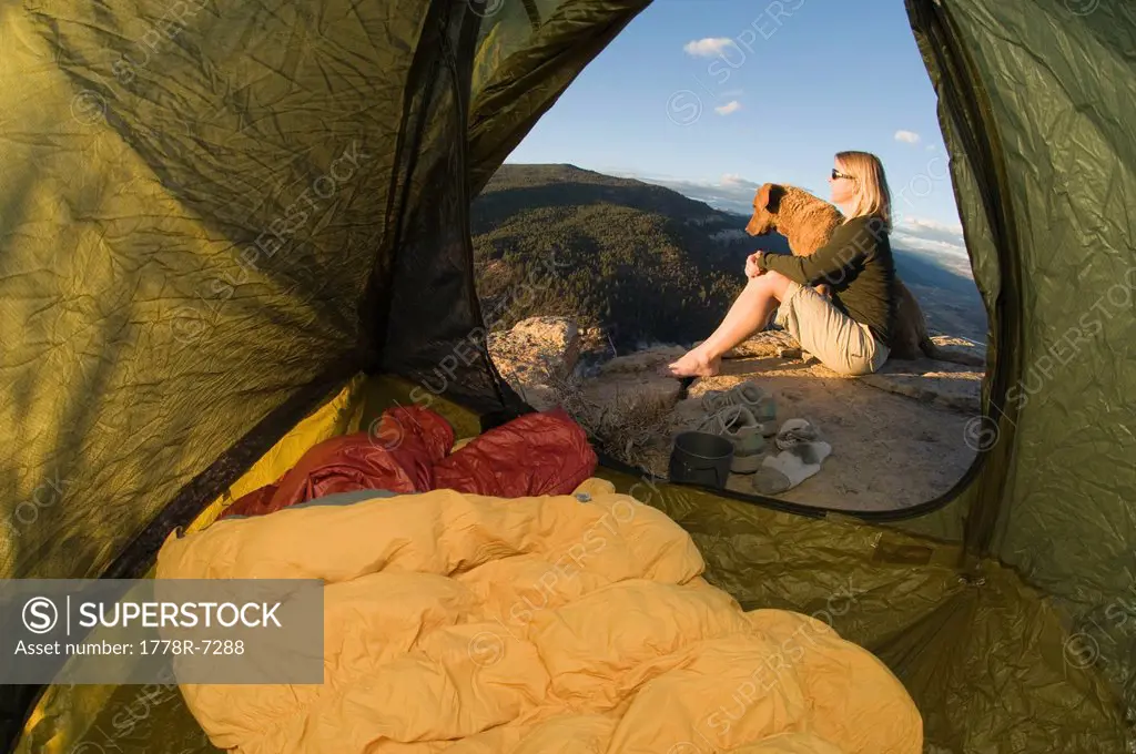 A woman and her dog sitting on rock watching the sunset while camping on Animas Mountain, Durango, Colorado.