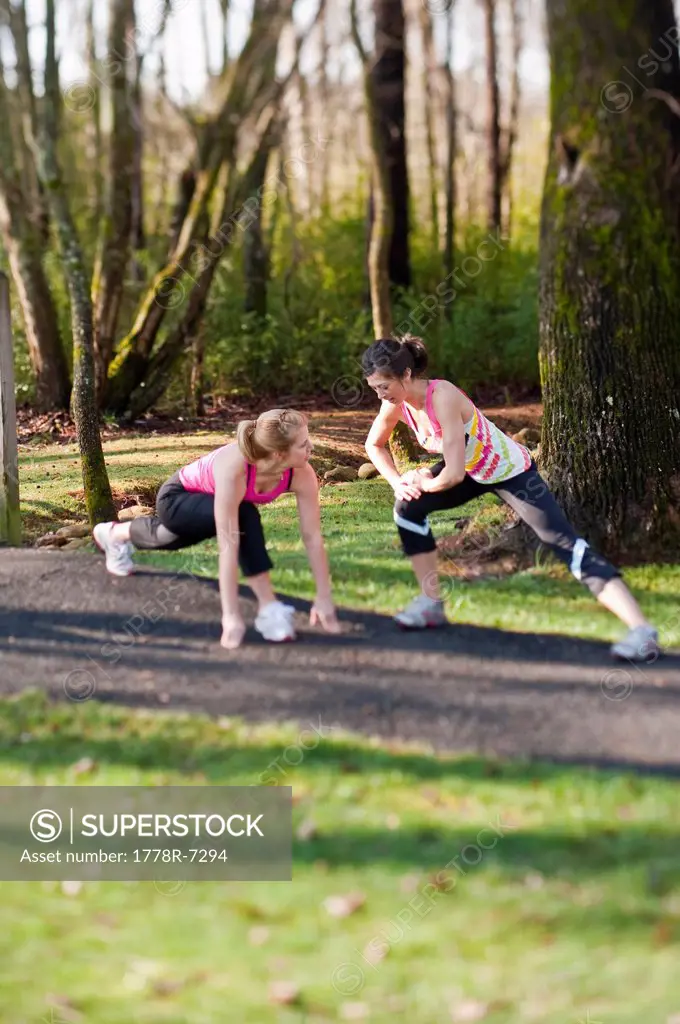 Two women in their mid_20´s stretching leg muscles outdoors.