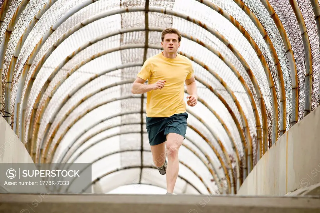 An athletic male jogging through a pedestrain overpass.