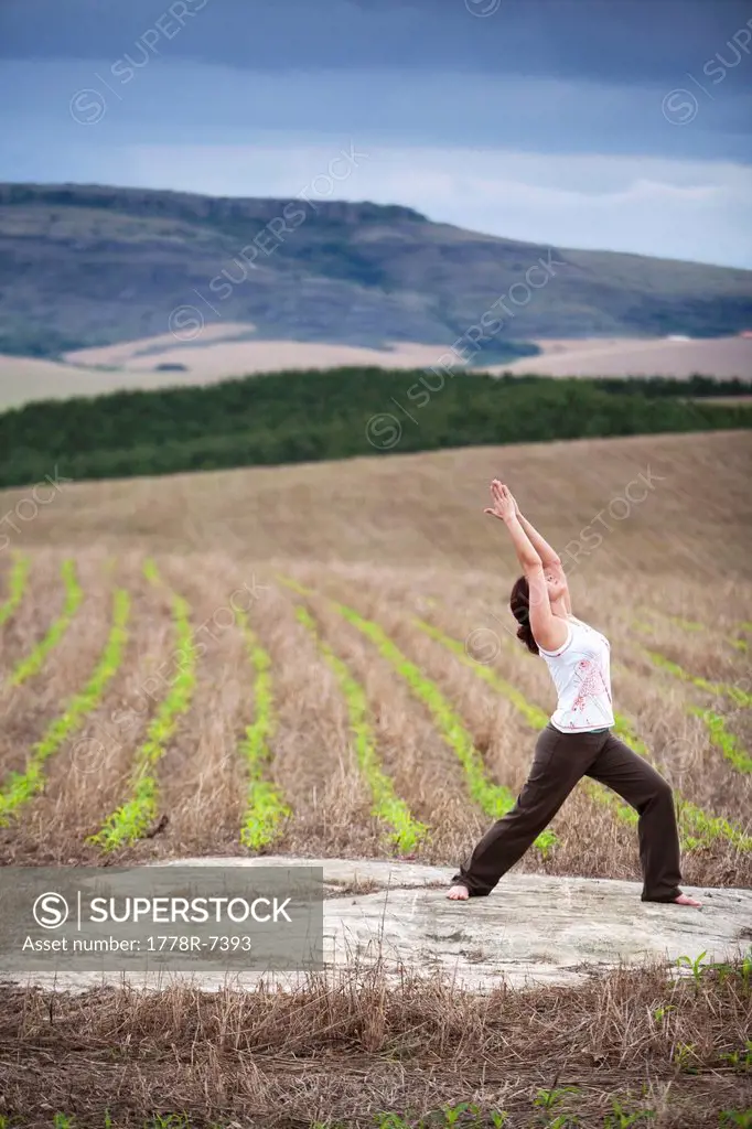 A woman practices yoga in a field under cloudy skies in Brazil.