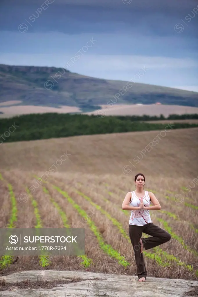A woman practices yoga in a field under cloudy skies in Brazil.