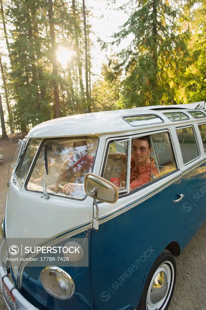 A young man and woman pose for a picture from inside their vintage van.