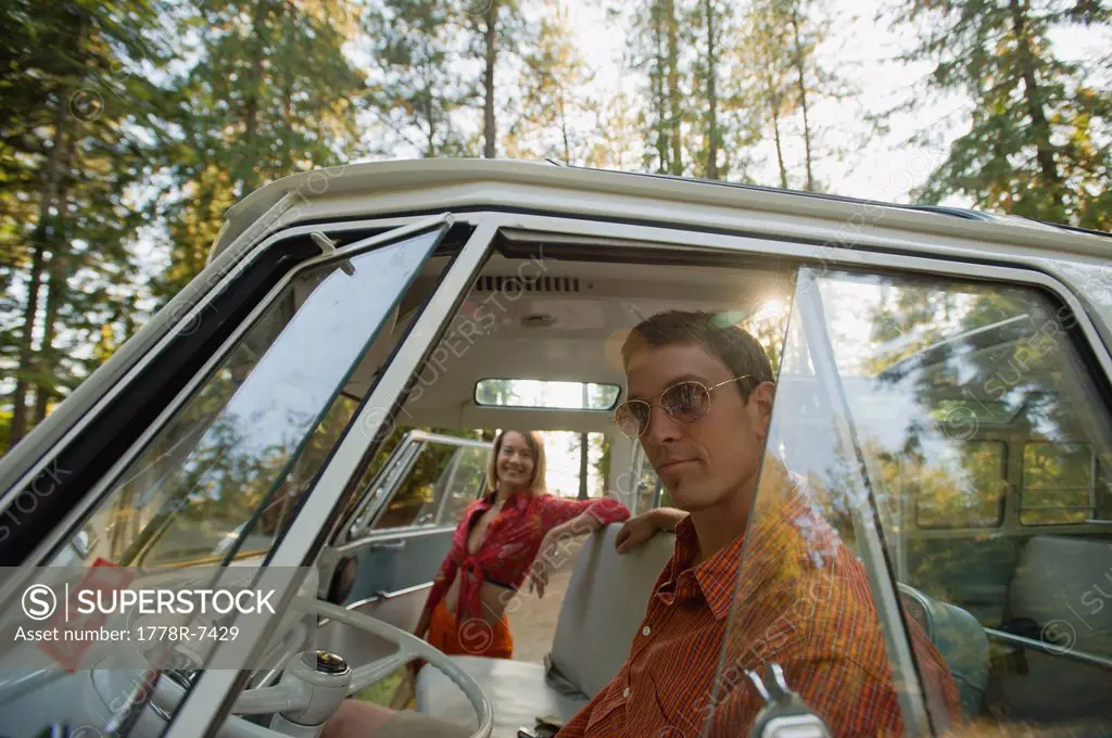 A young man in sun glasses offers a woman a ride in a vintage van.
