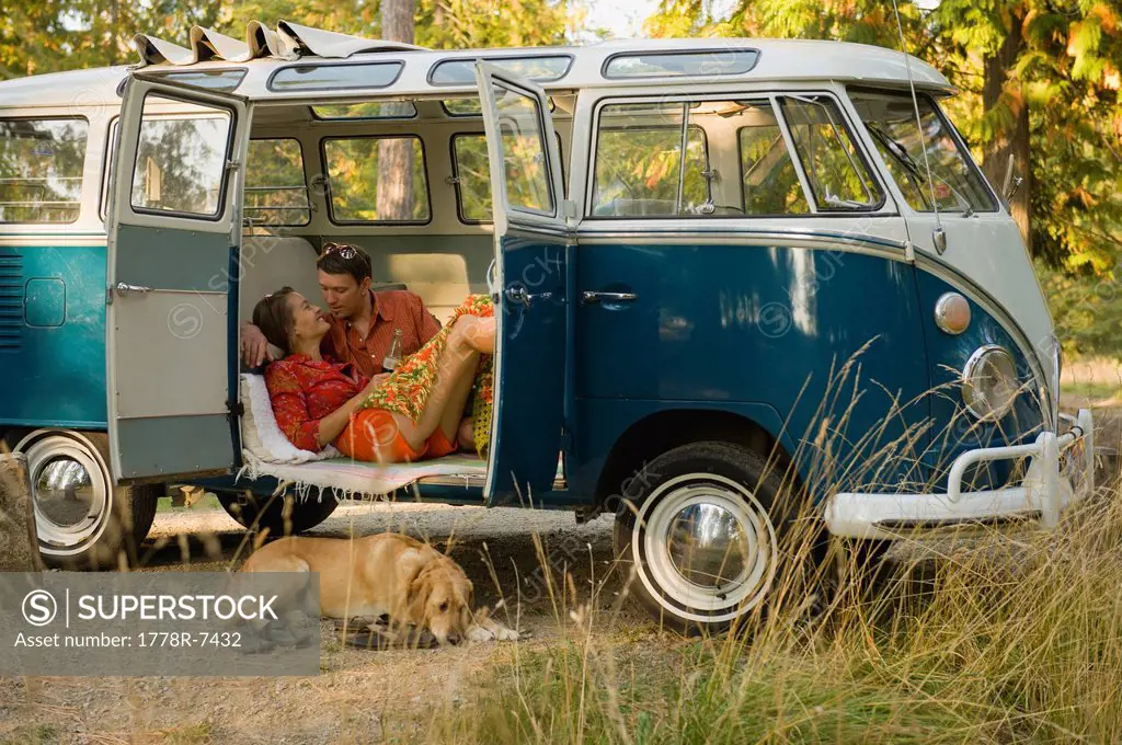 A young couple relax inside a classic van with their dog.