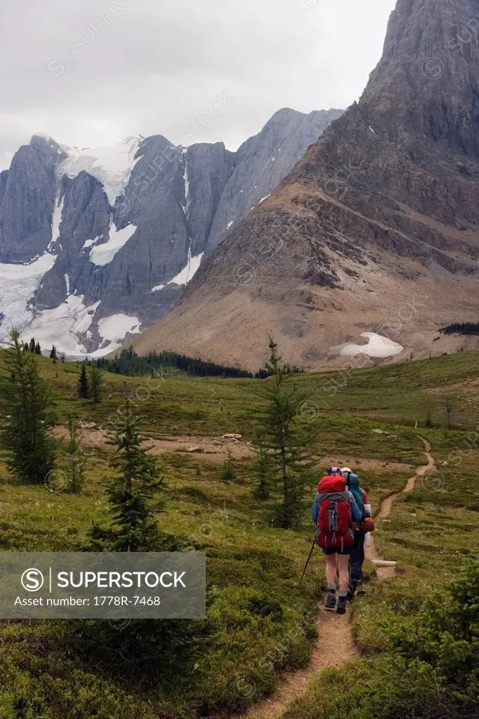 Two backpackers hike towards the towering limestone cliffs and glaciers of the Rockwall Trail, Kootenay National Park.