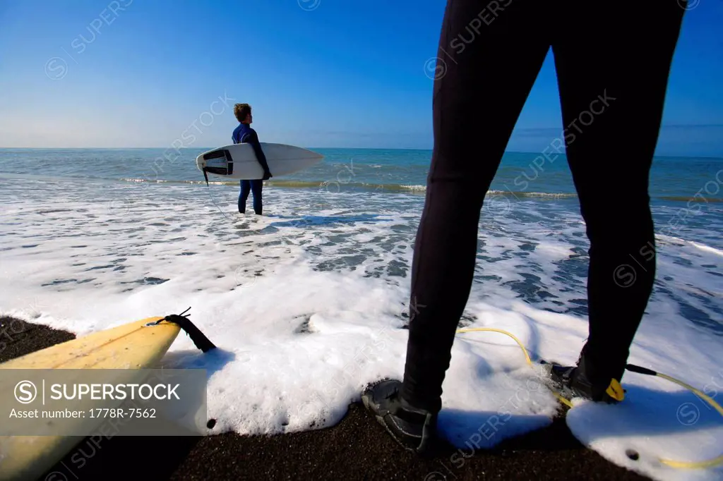 Two surfers stand on the beach on The Lost Coast, California.