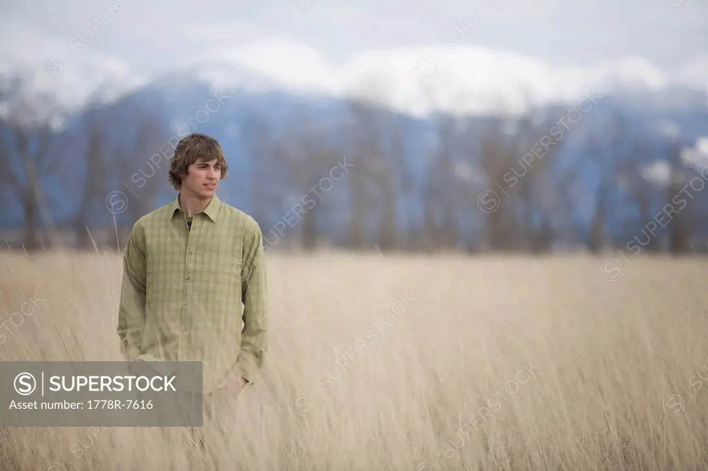 A young man enjoys a winter stroll through a field of grass with mountains in the background.