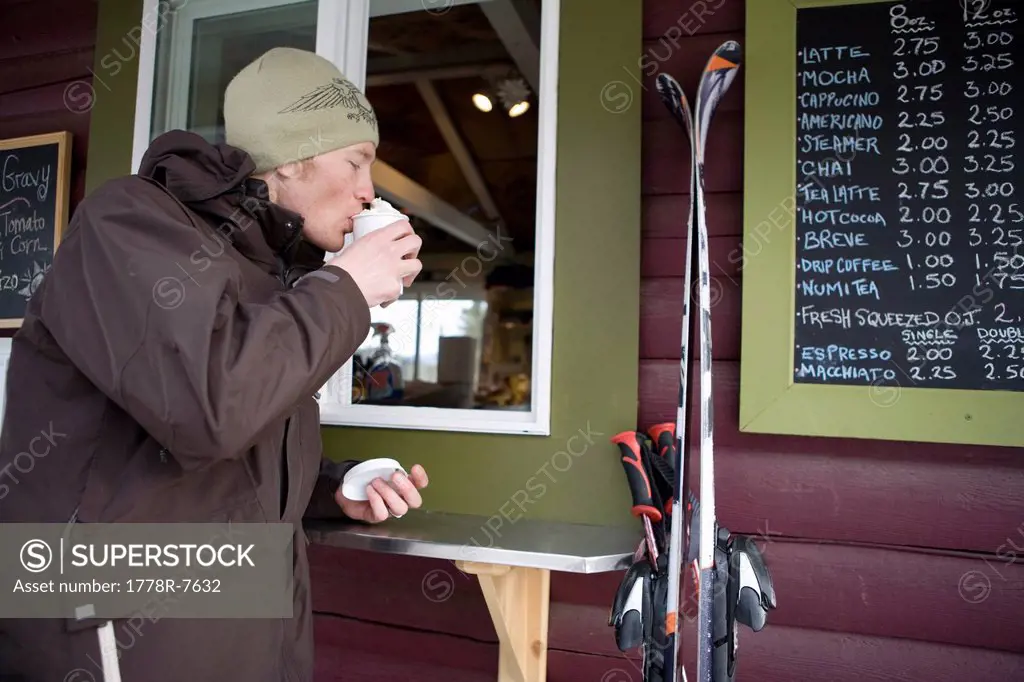 Twenty something male skier grabs a cup of coffee before skiing.