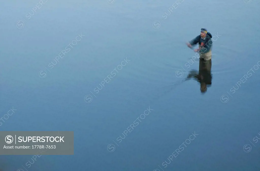 A young man fly fishes in flat, freezing cold water, on the Truckee River, California.