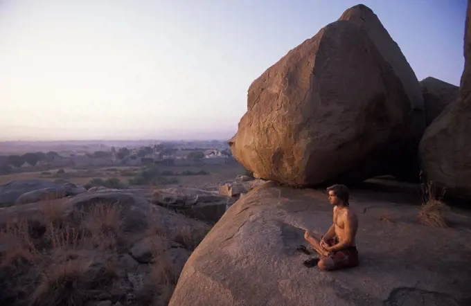 Male climber meditating at sunset in Hampi, India