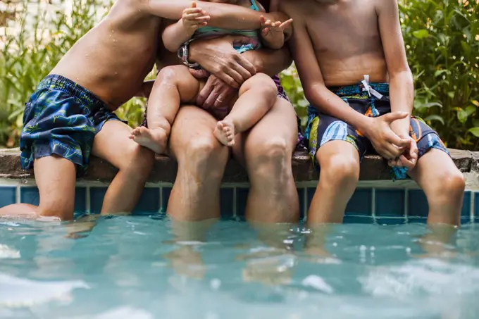 A Mother With Her Baby And Two Boys Sitting On A Pool Edge