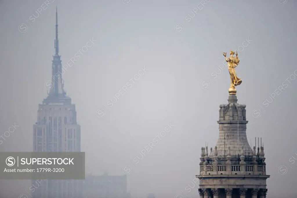 Golden statue on city hall with Empire State Building in fog