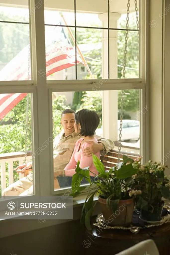 Hispanic military solder and wife sitting on porch swing
