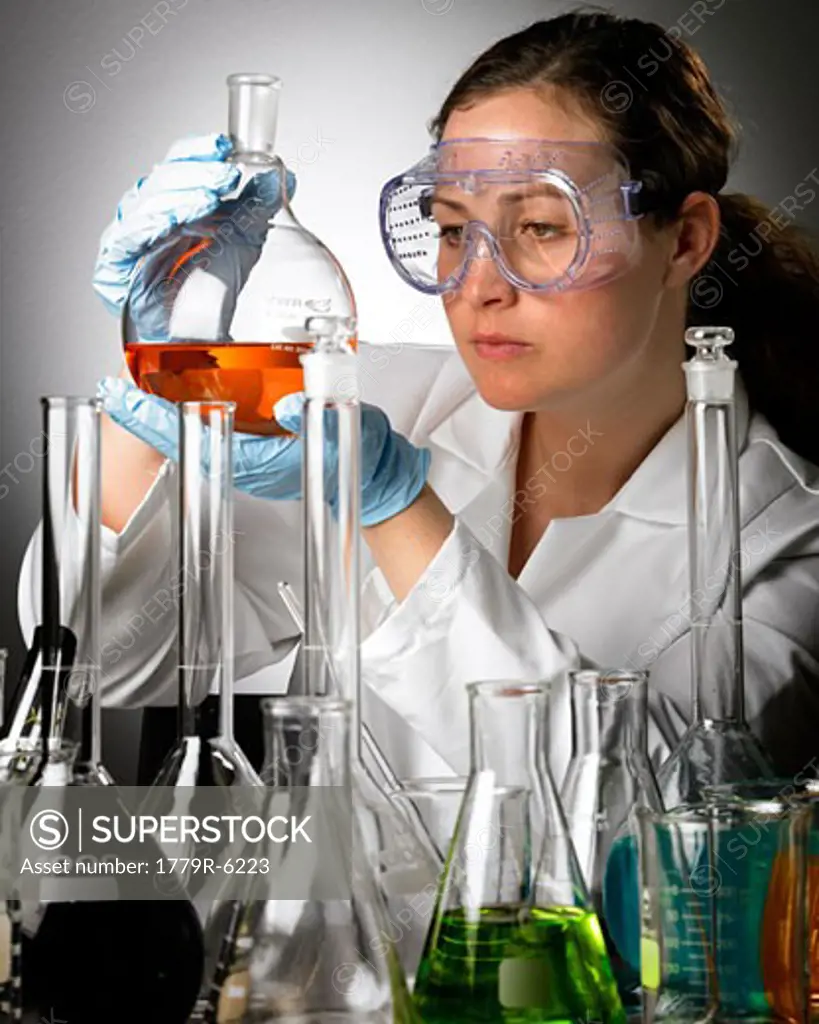 Woman in lab coat examining beaker of liquid
