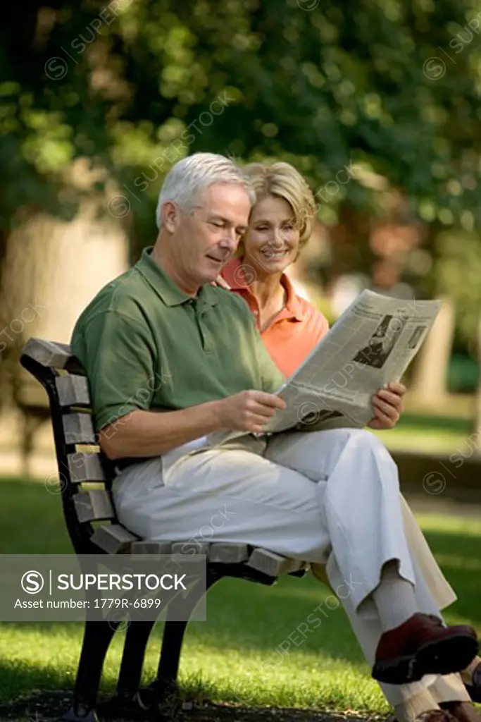 Senior couple on park bench reading newspaper