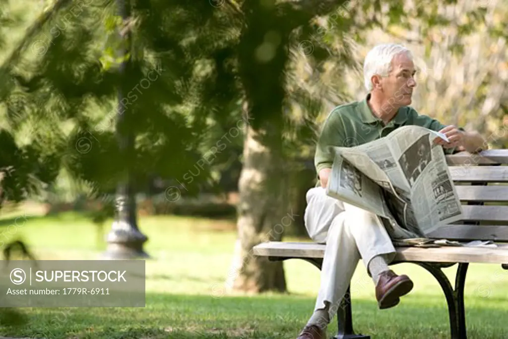 Senior man reading newspaper on park bench