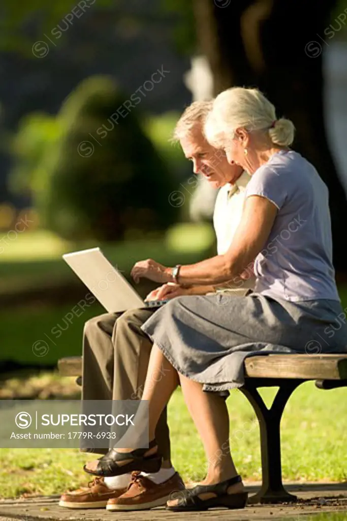Senior couple using laptop sitting on park bench