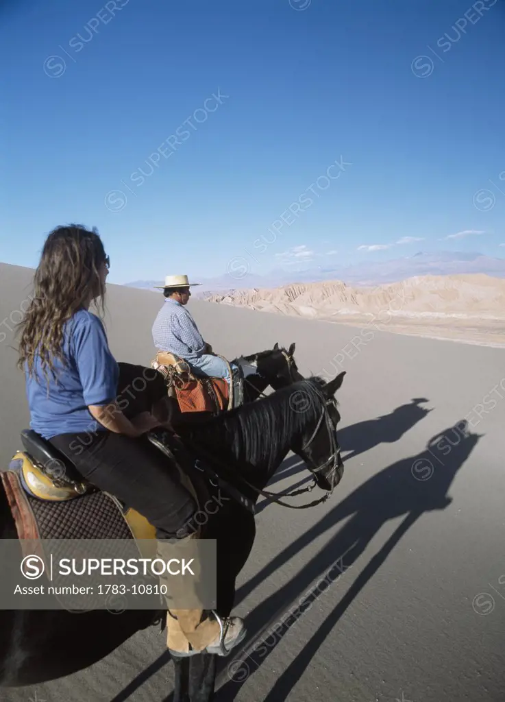 Couple horse riding in Valle de la Muerte, Cordillera De La Sal, Atacama Desert, Chile.
