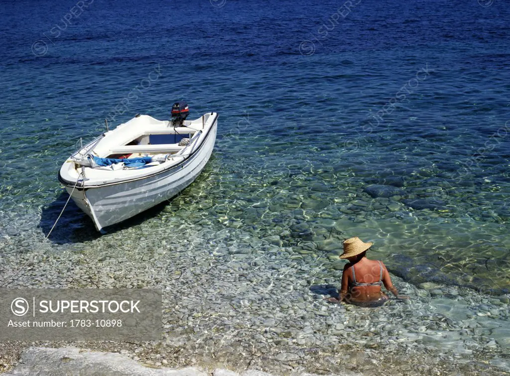 Woman wading in water next to boat, Corfu, North East Coast, Corfu, Greece