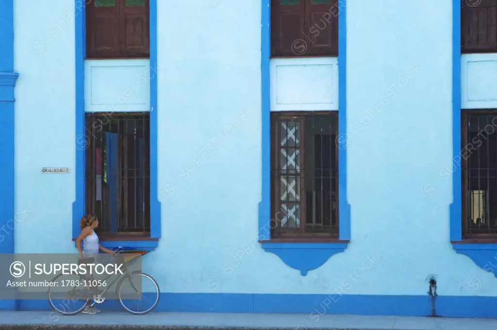 A woman with her bike outside a blue building in Bayamo. , Capital of Granma Province. Cuba.