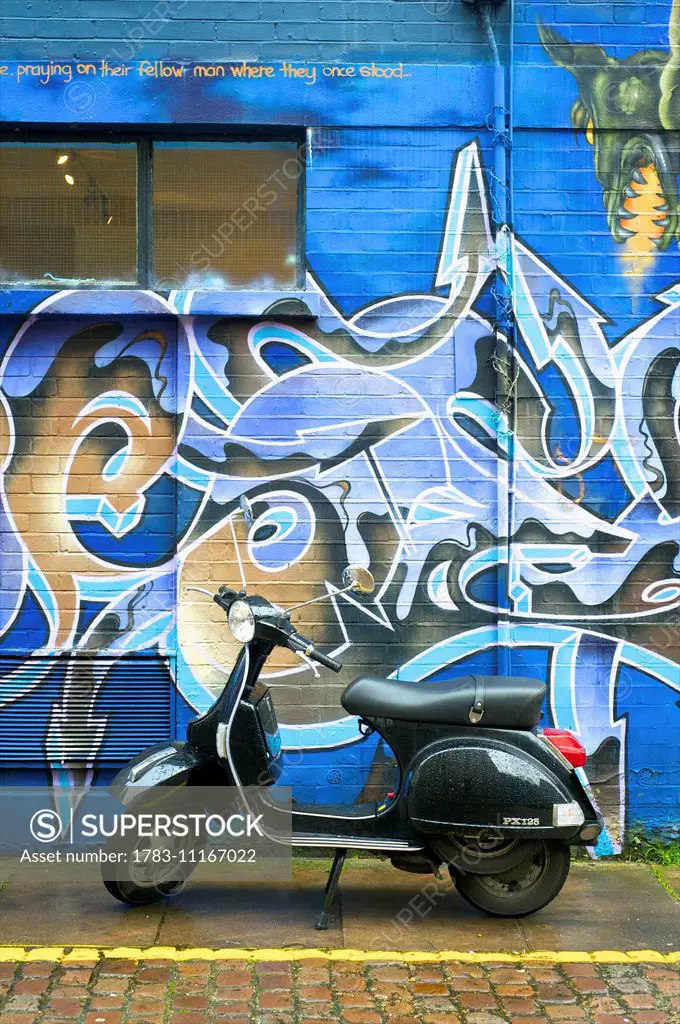 A motorized scooter parked outside a building with abstract artwork painted on the wall, Notting Hill; London, England