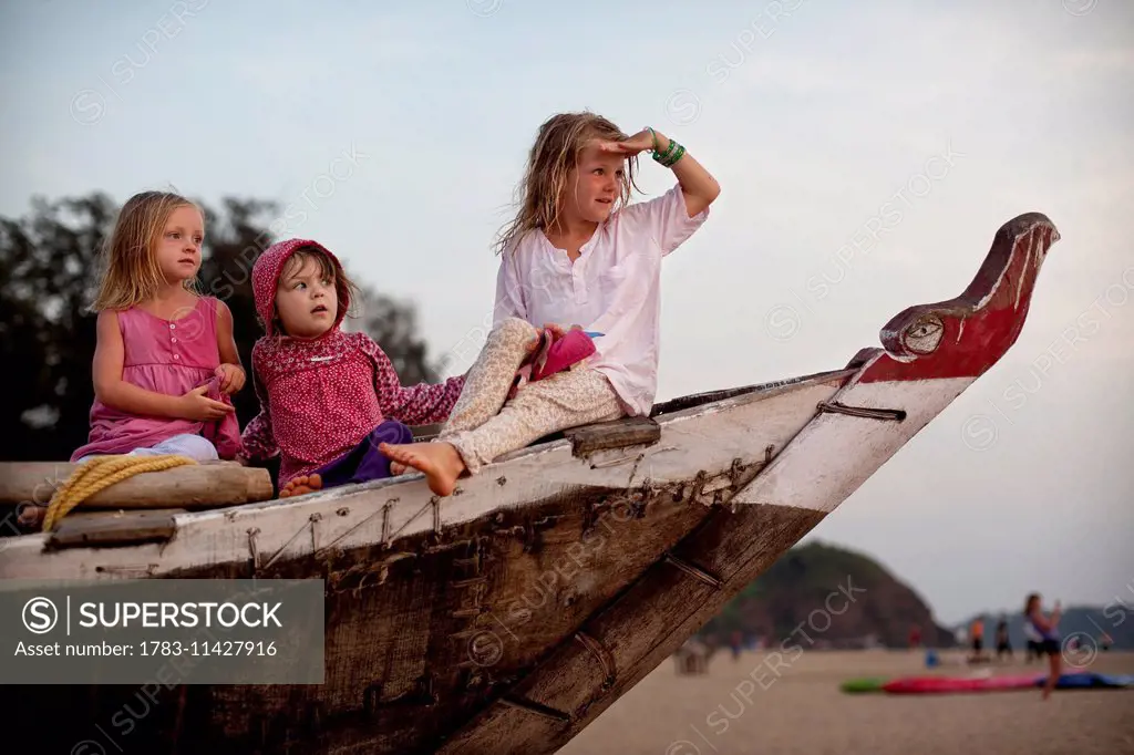 Girls play together on a traditional fishing boat on holiday in India, Patnum Beach, Goa, India.