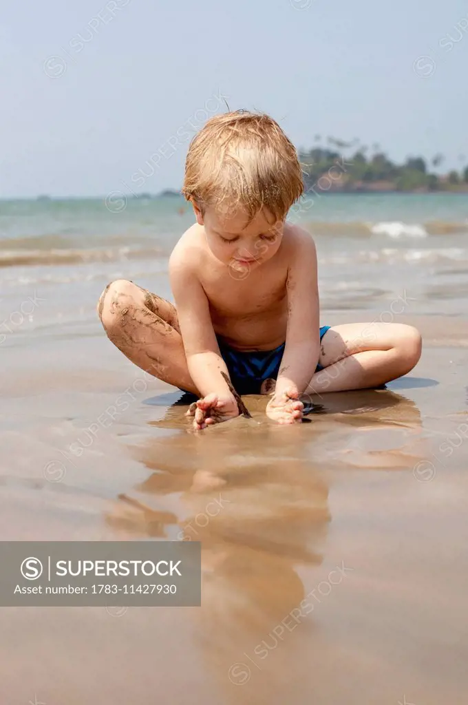 A boy plays with sand on Patnum beach, Goa, India.