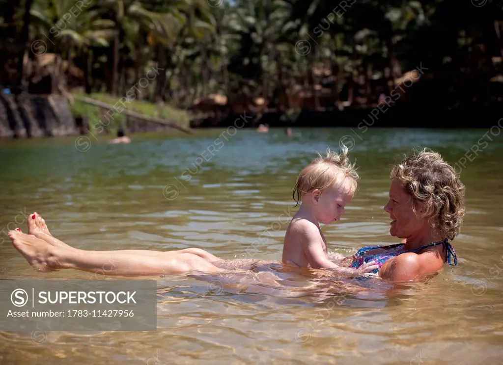 Mum and daughter enjoy swiming in the shallow fresh waters of the lagoon on Cola beach, Goa, India.