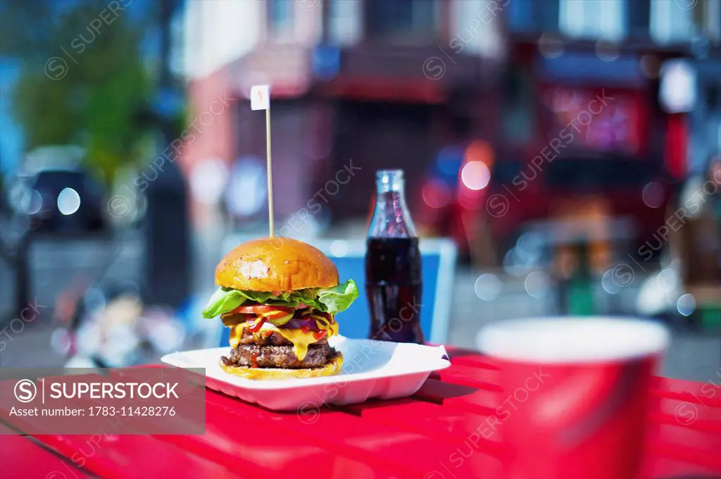 A large hamburger and bottle of pop on a table; London, England